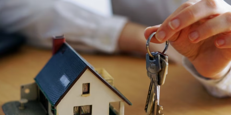 man holding keys next to a small model of a home